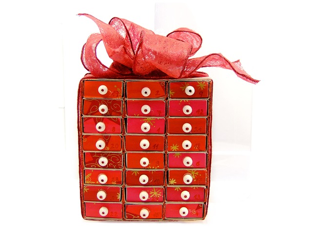 Un Calendrier de l'Avent original en forme de paquet cadeau avec des tiroirs rouges et roses numérotés, orné d'un ruban.