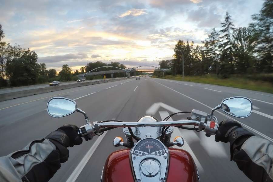 Vue subjective depuis le guidon d'une moto sur une grande autoroute au coucher du soleil, évoquant le départ vers des destinations en Europe à moto.