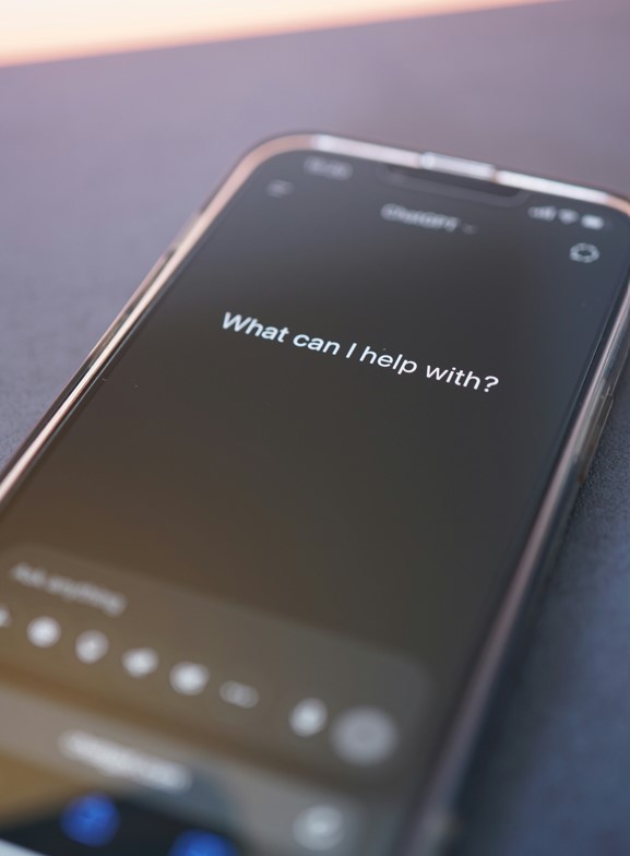 Un gros plan sur l'écran d'un smartphone affichant l'application ChatGPT avec la question "What can I help with?" sur un fond sombre, illustrant l'intégration du SEO intelligence artificielle dans les interfaces d'assistance conversationnelle.