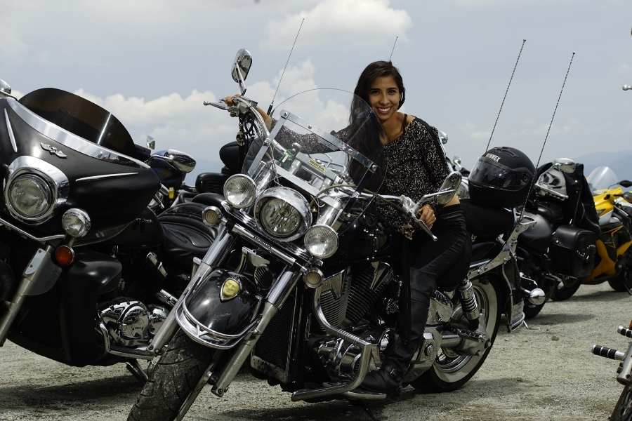 Une femme sourit en posant à côté d'une grande moto custom équipée d'une bulle de moto transparente.