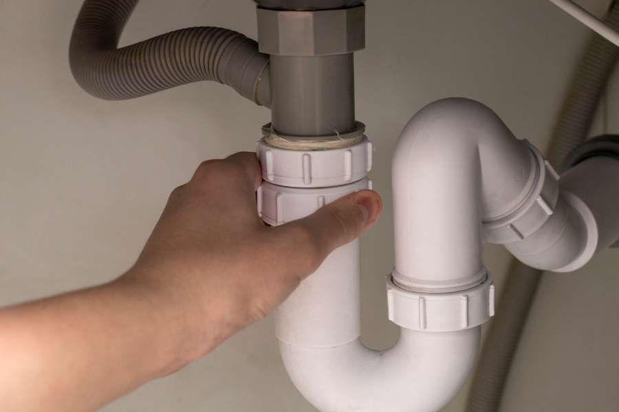 Une main serre les raccords de tuyaux de plomberie sous un évier.